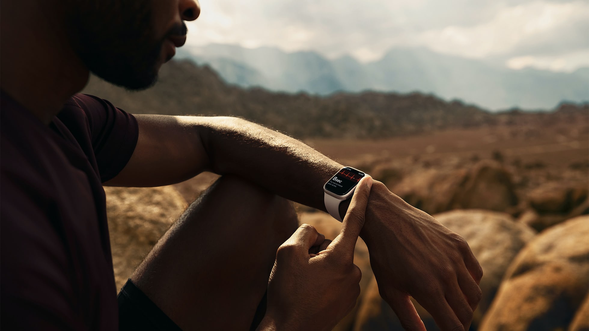 一名男子坐在沙漠中檢查他的 Apple Watch。